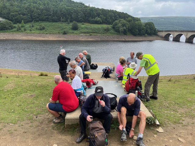 The group are sat around a raised concrete slab by the reservoir delving into backpacks and tying shoelaces
